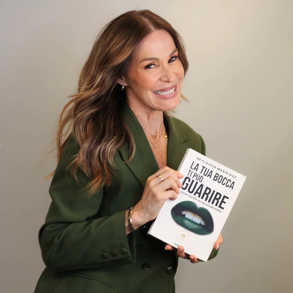 La Dra. Claudia Marín Díez sonriendo mientras sostiene su libro «La tua bocca ti può guarire»
